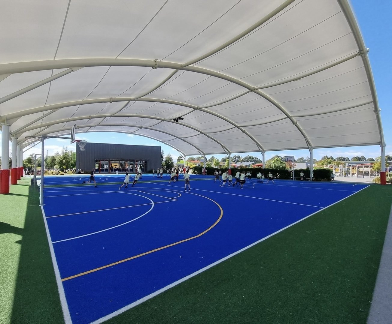 Large white fabric canopy with curved metal supports covering an outdoor sports court
