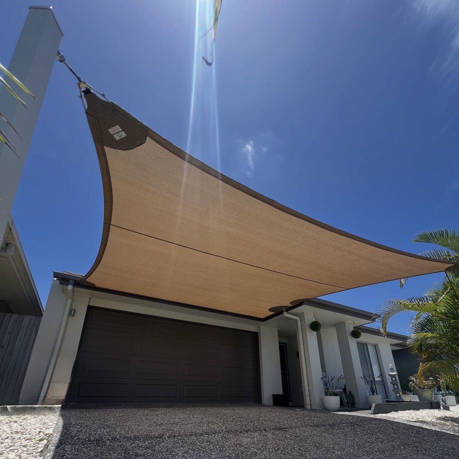 Beige outdoor shade sail providing sun protection over a modern villa courtyard