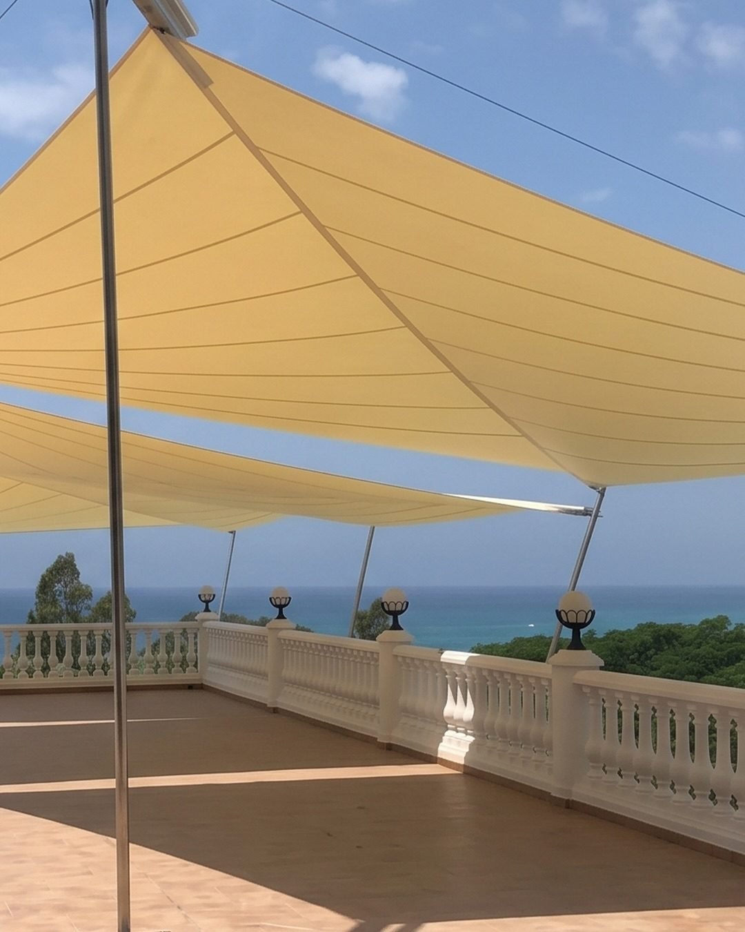Yellow tensile fabric shade canopy installed over an outdoor terrace with sea views